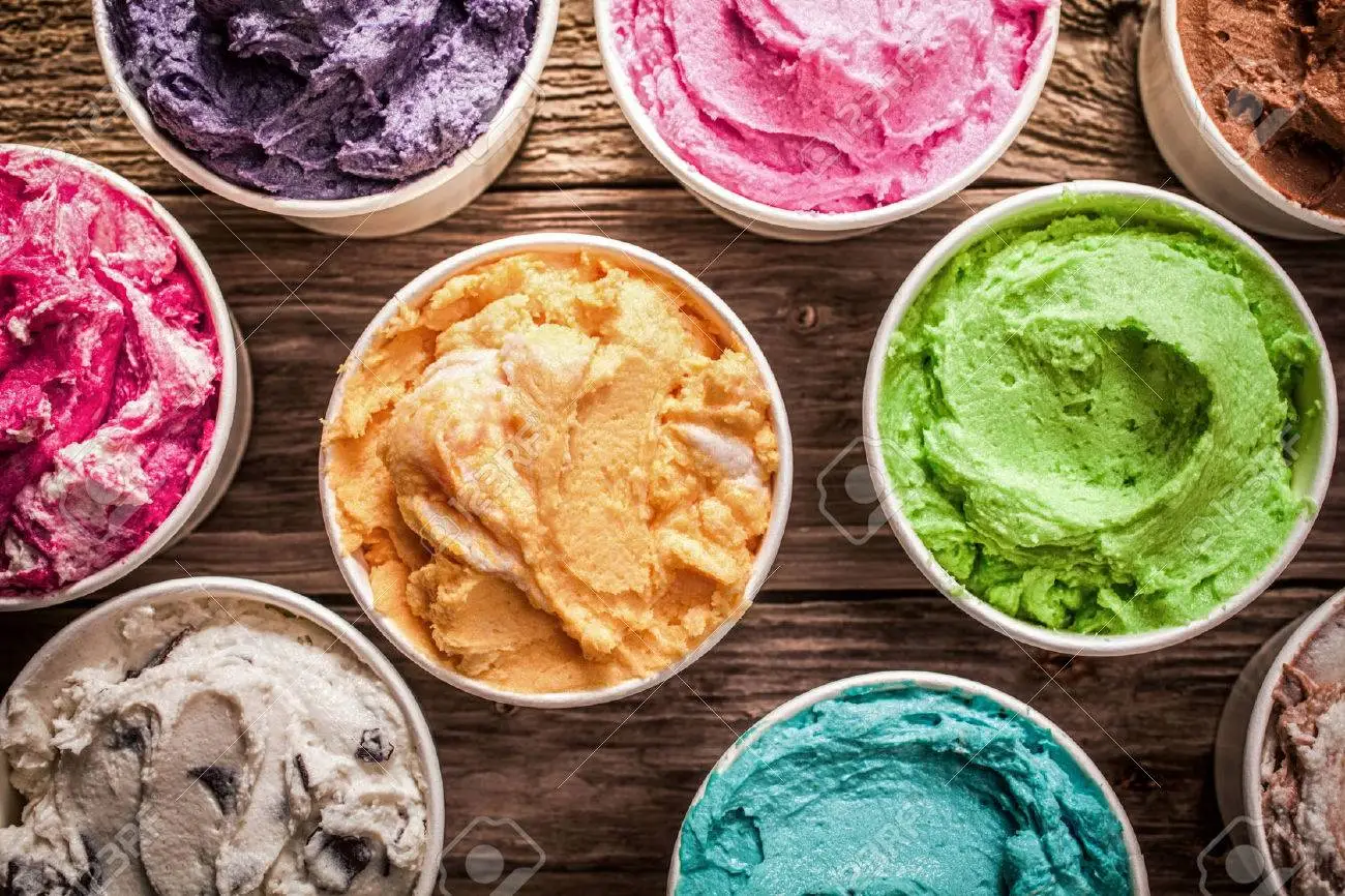 27128938 array of different flavored colorful ice cream in plastic tubs displayed on an old wooden table at a
